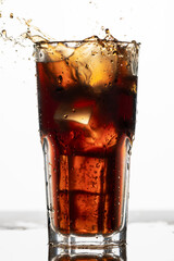 A splash into a glass of cola, a refreshing summer drink, cola with ice, frozen motion, macro