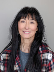 Fototapeta premium Portrait of a young woman with long black hair wearing a plaid shirt, standing against a gray background. Concept of casual fashion and natural beauty