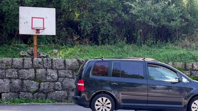Basketball hoop set on a street in Kotor, Montenegro, while a car passes by in the background – static video