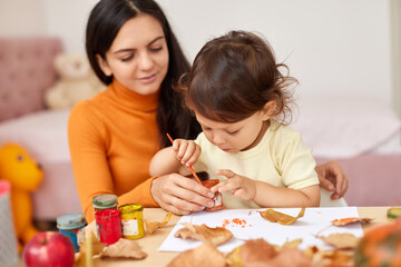 happy little child girl and her mother drawing for the autumn holiday. Happy family making autumn...