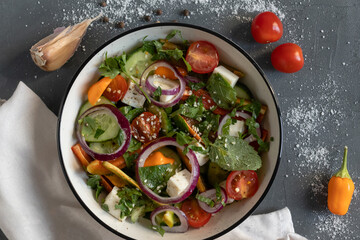 Spring salad with tomato, cheese, red onion and mint. On the background are ingredients, cherry tomato, yellow pepper and garlic. Healthy Food concept