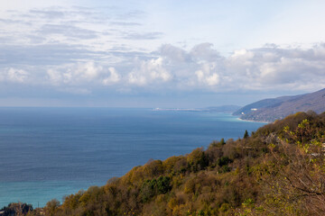 A breathtaking view from a mountain peak overlooking the sparkling sea on a sunny day. The clear blue sky and bright sunlight enhance the beauty of the coastline, creating a stunning panorama of