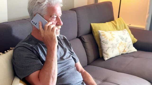 A mature man is captured on video sitting comfortably at home on the sofa, engaged in a phone conversation. His relaxed expression reflects the joy of staying connected with loved ones in his free tim