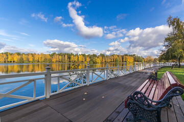 Obraz premium Wooden river embankment with white fences. Metal frame of a bench with a wooden seat. Beautiful landscape on a sunny day.