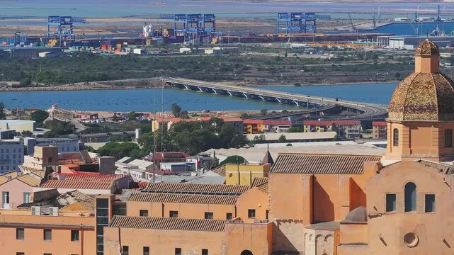 Vibrant aerial view of Cagliari, Sardinia, showcasing terracotta roofs, a bustling port, and the Mediterranean Sea with urban and natural landscapes.