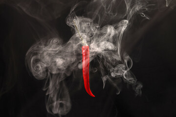 Smoking floating flying red hot birds eye chilli pepper on black background vapour fog mist move rotate swirl