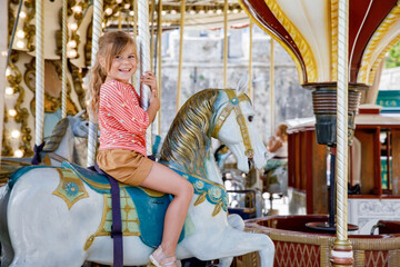 Happy positive preschool girl having a ride on the old vintage merry-go-round in city of St Malo...