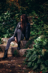 Woman, an adult and a beautiful brunette in a leather jacket and jeans, walks in the park in autumn.
