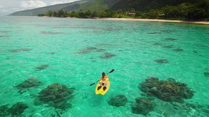 Aerial view of a young woman enjoying paddleboarding in a stunning tropical lagoon with turquoise water, surrounded by a lush green coastline © Anastasia Pro