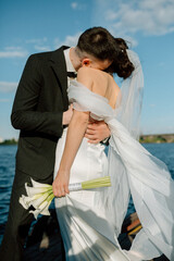 Bride and groom holding hands, hugging and kissing. Love concept. Elegant wedding couple on the river side in sunlight