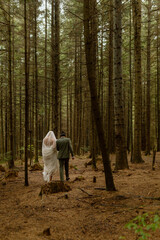 Fototapeta premium Wedding couple walks through the rainy fogy forest. Bride and groom walks holding hands in autumn forest