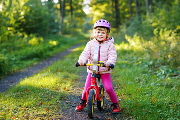 Child riding balance bike. Kids on bicycle in sunny forest. Little girl enjoying to ride glider bike on warm day. Preschooler learning to balance on run bicycle in safe helmet. Sport activity