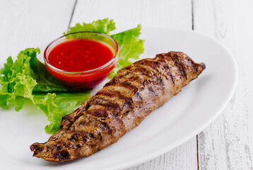 Delicious grilled steak lying on white plate with lettuce and red sauce