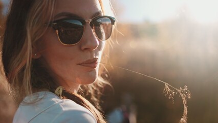 Young woman wearing sunglasses is chewing on a piece of grass while enjoying a beautiful sunset in the carpathian mountains of ukraine