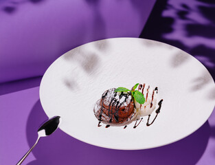 Chocolate fondant with vanilla ice cream decorated with mint leaves on white plate on purple...