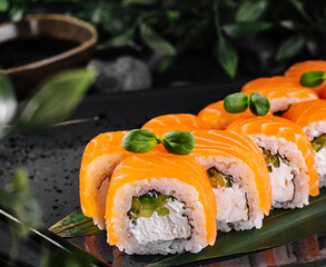 Philadelphia sushi rolls covered in salmon and decorated with greens being served on black plate