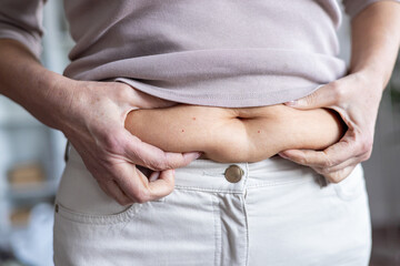 Close-up image showing person pinching belly fat with both hands, symbolizing weight concerns, body...