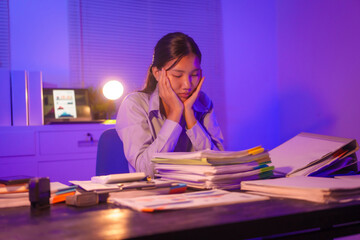 young Asian business trainee works late at her desk, typing on a laptop. Overwhelmed by stress and deadlines, she feels the weight of overtime, battling exhaustion and pressure in the quiet night.