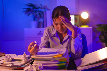 young Asian business trainee works late at her desk, typing on a laptop. Overwhelmed by stress and deadlines, she feels the weight of overtime, battling exhaustion and pressure in the quiet night.