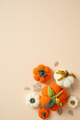 Handcrafted crochet pumpkins with wooden leaves on a light peach background. Flat lay, top view.