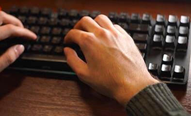an overhead view of the hands of a young programmer working on a keyboard on a wooden table. The concept of remote work or study