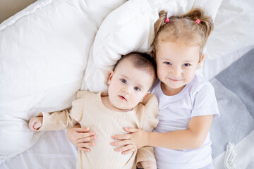 two sisters' children cuddle on the bed at home, the older sister holds the baby at home on the bed, the sisters' love and friendship in the family