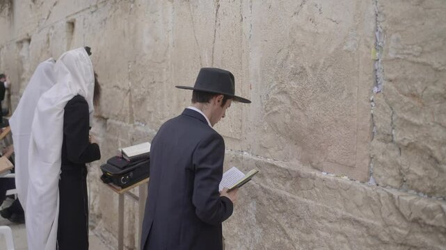 Jewish Prayer at Western Wall, Jerusalem, Israel. Religious men rock backwards and forwards and side to side while praying. Some wear black suits and hats. Others wear while shawls and phylacteries.