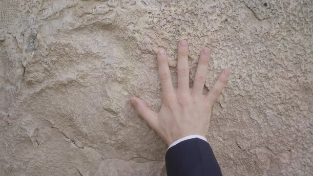 Jewish Prayer at Western Wall, Jerusalem, Israel. A religious man places his hand on the wall. The brim of his black hat is seen and it rocks in and out of frame as he recites the prayers.