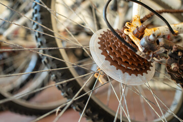 Detailed shot captures rusty gears on bicycle tire during daytime, showcasing intricate mechanism coated with rust, texture of gears contrasts with spokes and rubber tire 