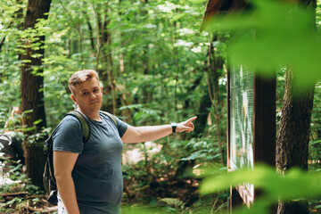 Happy traveler man pointing on wooden billboard in the nature. Portrait of young handsome man with...