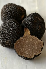 Fresh black truffles on a wooden surface, one sliced to reveal its rich interior.
