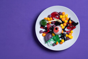 Assortment of Halloween candies isolated on purple background. Top view. Copy space