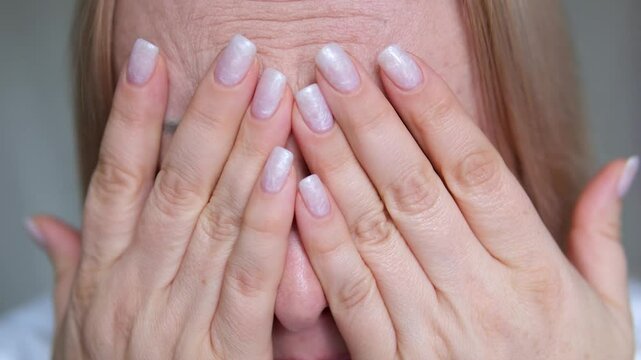 blonde adult woman hides behind hands close eyes with hands look out make sad look cry but then laugh deceive emotions