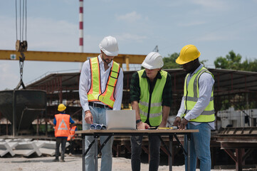 Multi-ethnic workers wearing hard hats in Engineering Workshop. Three industrial workers in hard hats are conversing on the storeroom floor.