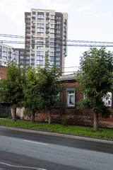 Obraz premium Old dilapidated hut, trees along the road. Modern skyscraper in the background. Power lines. Eclectic architecture on the streets of Ufa. Bashkortostan