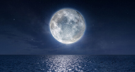 Full moon rising above ocean and casting shining reflection on water at night.