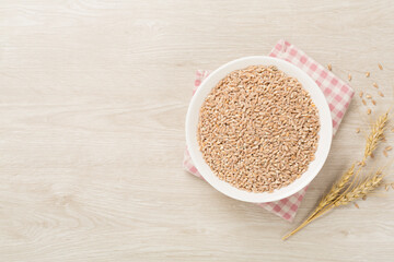 Bowl with spelt grain on wooden background, top view