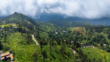 Obraz premium Lush Sri Lanka hills beneath clouds. An expansive view of the green hills of Sri Lanka, showcasing winding roads and scattered villages beneath a cloudy sky.