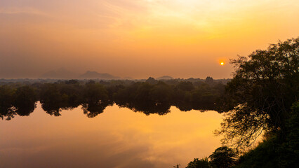 Sunset reflection over serene water in Sri Lanka. A tranquil sunset casts vibrant colors across the water, reflecting the lush greenery and distant mountains of Sri Lanka.