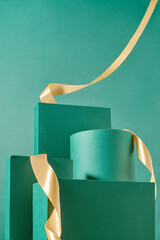Three green square podiums and one cylindrical podium against a green background. A yellow ribbon...