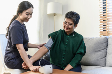 Young Asian woman nurse take care senior woman at nursing home, checking blood pressure for observe...