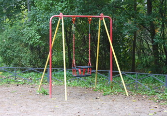Fototapeta premium A children's swing stands near green bushes surrounded by a low fence
