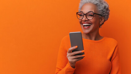 Joyful Senior Woman Using Smartphone Against Vibrant Orange Background, Embracing Technology and Connectivity