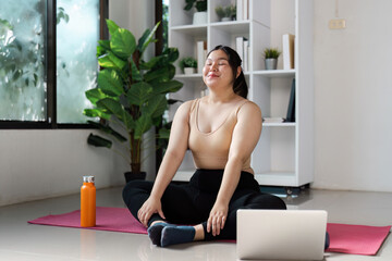 Confident Overweight Woman Practicing Yoga at Home with Laptop and Water Bottle in Bright Living Room