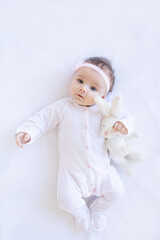 baby girl smiling on the bed on a white cotton bed with a toy falling asleep or waking up in the morning, cute newborn little baby at home on an isolated background close-up