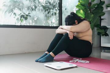 Contemplative Woman Sitting on Yoga Mat Next to Scale in Bright Room with Green Plants