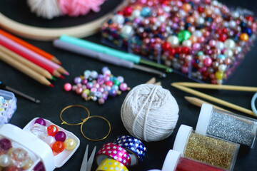 Colorful beads, coloring pencils, glitter, needles, string, hoop, tape and scissors on dark...