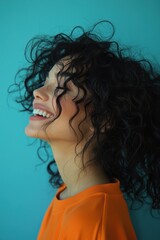 Naklejka premium Profile shot of a woman with dark curly hair in vibrant orange shirt against a blue background, exuding happiness and energy