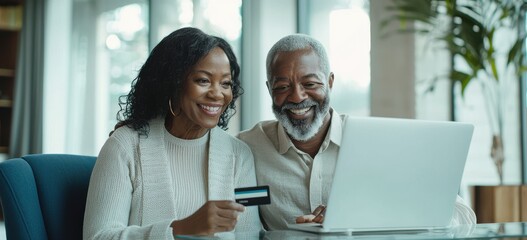 Senior Black couple smiling while holding a credit card and using a laptop in a modern office setting