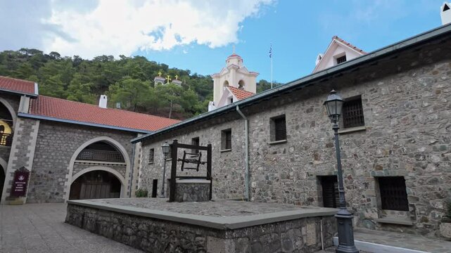 Historic Kikkos Monastery courtyard with stone buildings and a bell tower on a sunny day